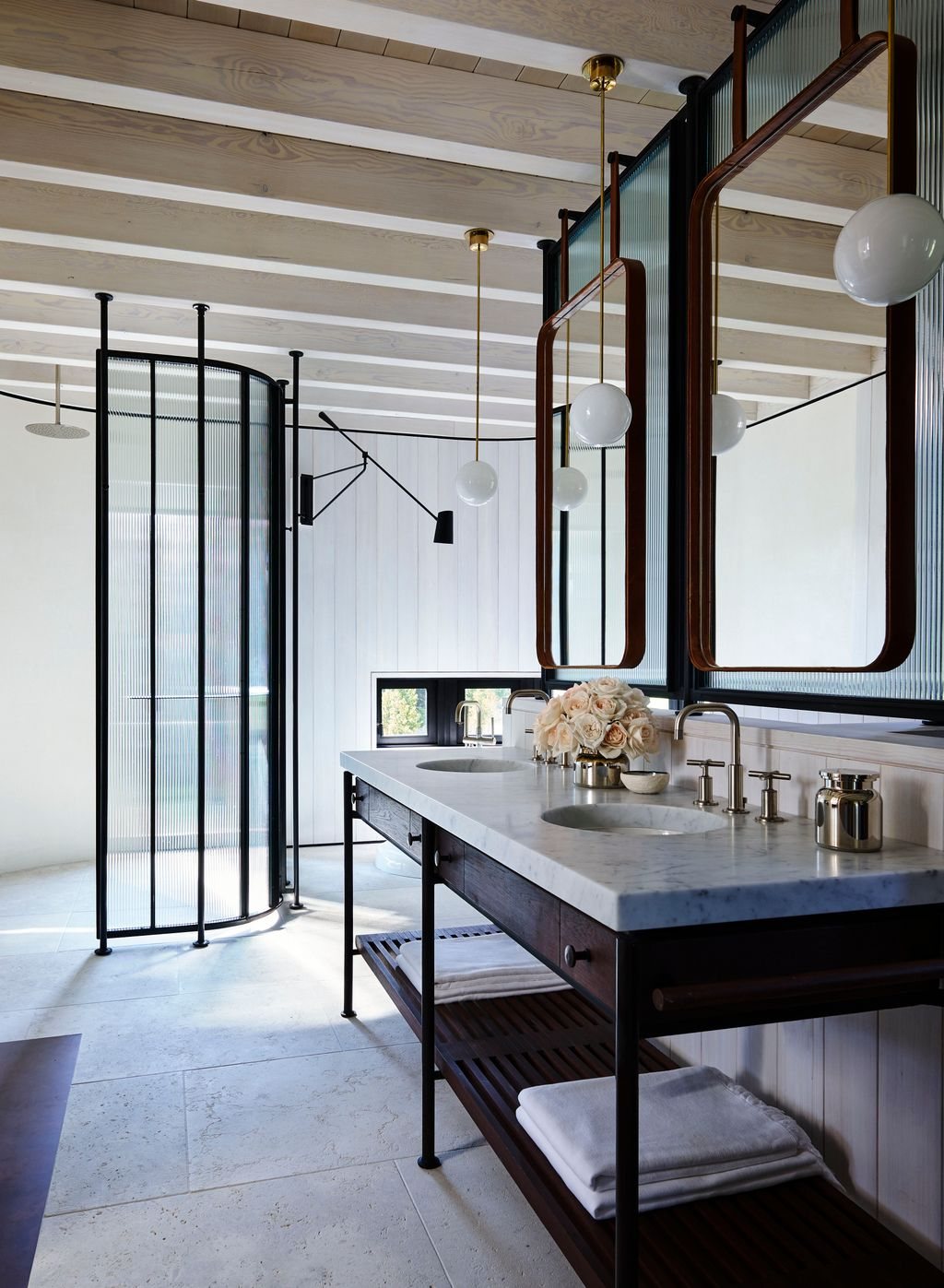 A serene bathroom with warm wood cabinetry, pale stone and a glass shower